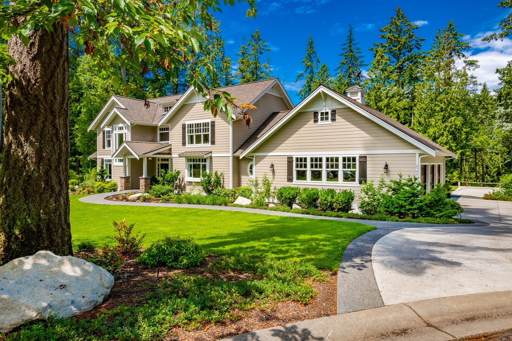 Beautiful custom built craftsman style home three car garage with wooden doors lush landscaping with spring foliage and shadows dappling the yard