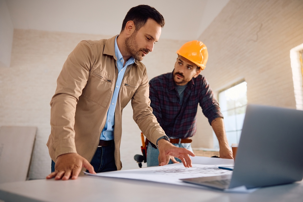 Home owner analyzing blueprints with a worker during renovation process.
